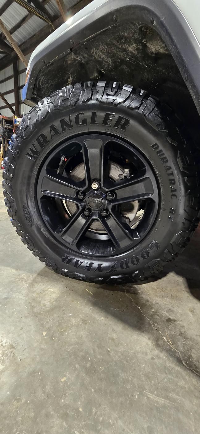 A Goodyear Wrangler DuraTrac tire mounted on a black wheel inside the shop